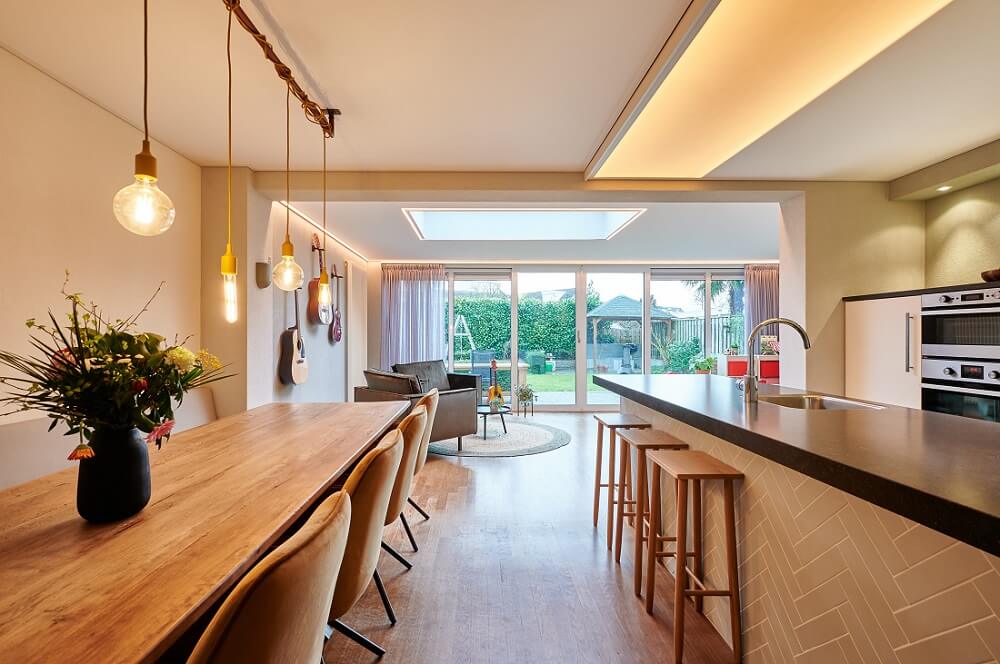 Plameco spanplafond: keuken met aangrenzend ewoonkamer: lichtmodule met Human Centric Lighting boven het kookeiland, hanglampen boven de eettafel en integreerde LED-lijn in de plafondrand in de woonruimte.